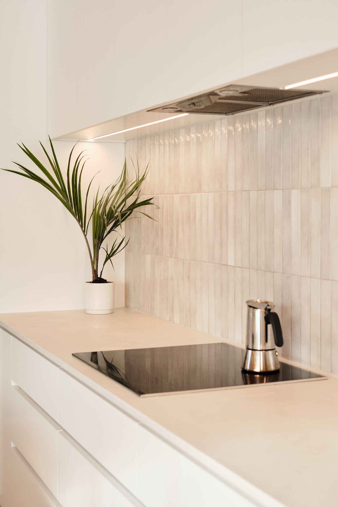 Kitchen bench and cooktop with white tiles and white cabinetry